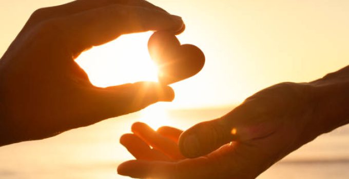 Hand passing heart to another.